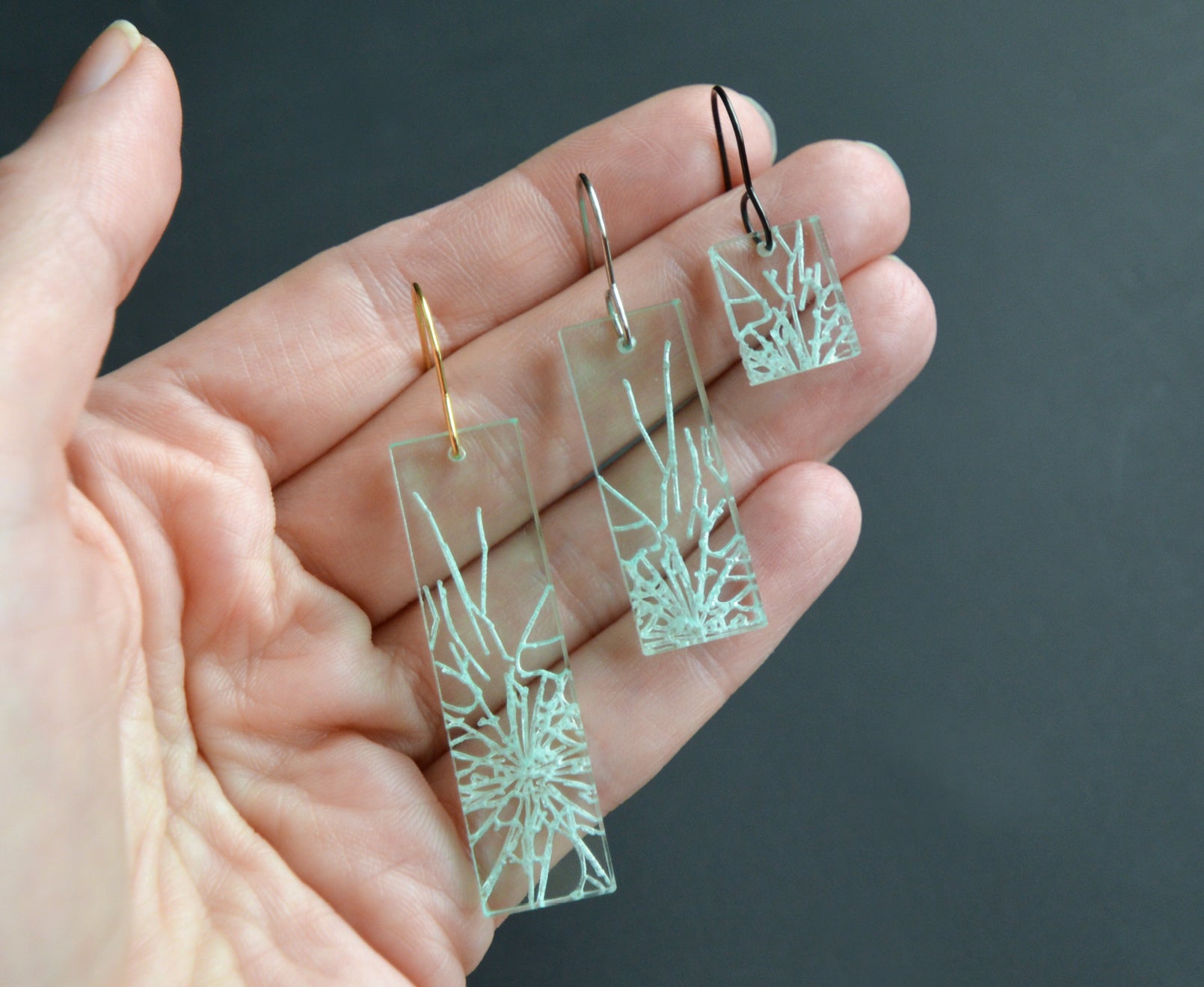 Statement earrings with shattered glass appearance, representing breaking the glass ceiling, 3 different lengths and metal colors sitting in the palm of a hand.