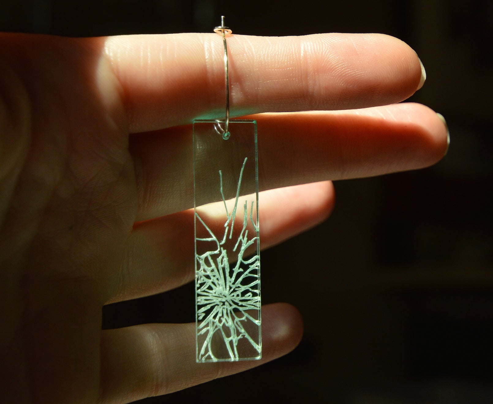 Glass ceiling earring with light shining through, held up by a hand.