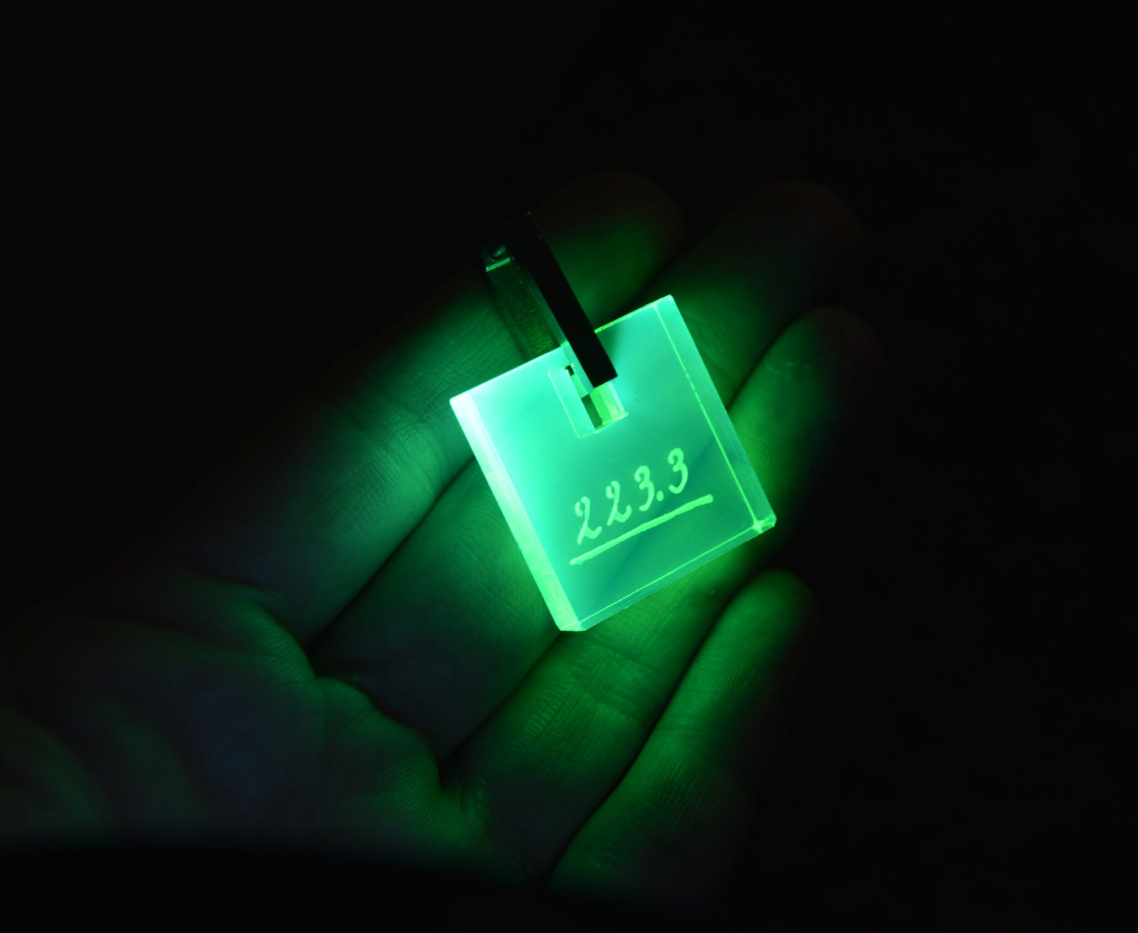 Neon acrylic earrings engraved with Marie Curie’s handwriting and the atomic weight of radium, glowing under blacklight with stainless steel leverbacks.