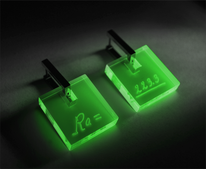 Neon acrylic earrings engraved with Marie Curie’s handwriting and the atomic weight of radium, glowing under blacklight with stainless steel leverbacks.